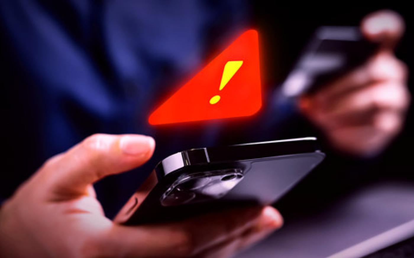 A person holding a smartphone and credit card with a glowing red warning symbol above the phone.