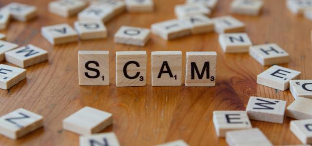 Scam spelled with scrabbles on a wooden table by Markus Winkler courtesy of Unsplash.